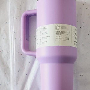 Puede incluir: Un vaso t&eacute;rmico aislado de color lavanda con asa y tapa transparente. El vaso tiene un borde de acero inoxidable y una pajita transparente. Una etiqueta lateral proporciona informaci&oacute;n del producto. Est&aacute; dise&ntilde;ado para mantener las bebidas fr&iacute;as.