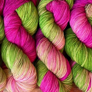 Könnte beinhalten: Nahaufnahme mehrerer Garnknäuel in leuchtenden Farben. Das Garn ist eine Mischung aus leuchtendem Pink und Limettengrün, was einen auffälligen Kontrast erzeugt. Das Garn ist eng gewickelt und zeigt die Textur der Fasern. Ideal für Strick- und Häkelprojekte.