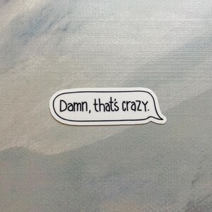 May include: A white sticker with a black border and the text "Damn, that's crazy" in a speech bubble. The sticker is on a light blue and white background.
