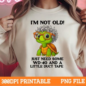 May include: Cream-colored sweatshirt featuring a cartoon turtle with glasses and gray hair. The turtle has a green face and shell, with the text "I'M NOT OLD! JUST NEED SOME WD-40 AND A LITTLE DUCT TAPE". The bottom of the image has the text "300DPI PRINTABLE PNG FILE".
