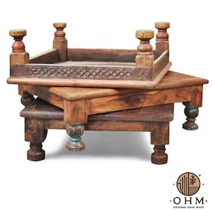 Pode incluir: Duas mesas quadradas de madeira empilhadas com acabamento castanho escuro e textura desgastada. Cada mesa apresenta quatro pernas esculpidas com pés arredondados e um padrão de treliça decorativo nas bordas laterais. O logótipo OHM ORIGINAL HAND MADE é visível.