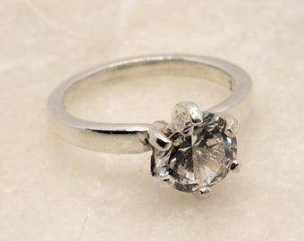 May include: A silver ring with a clear, round gemstone set in a prong setting.