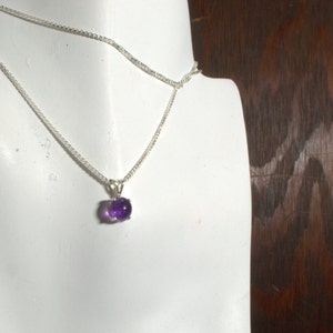 May include: A silver chain necklace with a small, oval-shaped amethyst pendant.