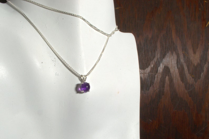 May include: A silver chain necklace with a small, oval-shaped amethyst pendant.