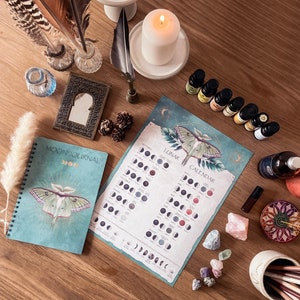 Pu&ograve; includere: Un diario lunare blu e verde con un'illustrazione di falena e il testo "Moon Journal" sulla copertina. Un calendario lunare con un'illustrazione di falena e il testo "Lunar Calendar" &egrave; su una superficie di legno con vari cristalli, oli essenziali e altri oggetti di stregoneria.
