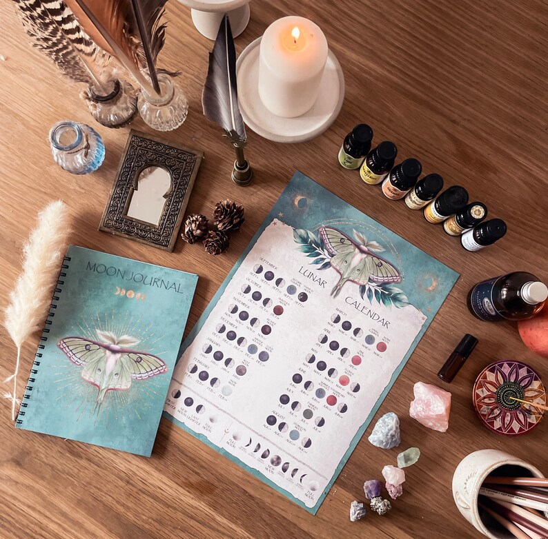 Pu&ograve; includere: Un diario lunare blu e verde con un'illustrazione di falena e il testo "Moon Journal" sulla copertina. Un calendario lunare con un'illustrazione di falena e il testo "Lunar Calendar" &egrave; su una superficie di legno con vari cristalli, oli essenziali e altri oggetti di stregoneria.