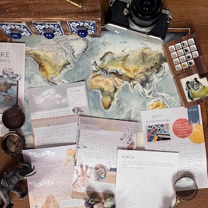 May include: A watercolour world map with a light blue background and brown continents. The map is surrounded by various items, including a compass, a wooden box with compartments, a camera, a magnifying glass, and several colourful stones. There are also several printed cards with information about Africa, including a map of Africa, a picture of a zebra, and a picture of a lion. The text on the cards reads "Africa", "Read", "Think", "Explore", "Artist: Esther Mahlangu", and "Born 1 November 1935 in Middelburg, Mpumalanga, South Africa".