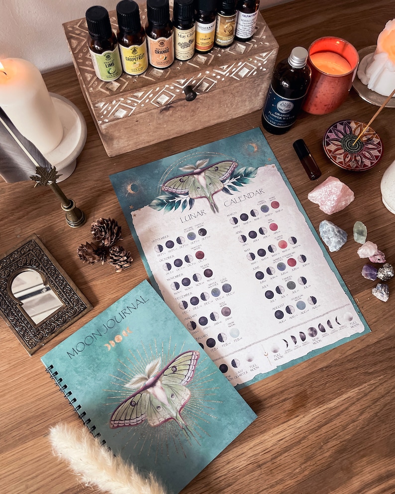 Pu&ograve; includere: Un diario lunare blu-verde con un designo di falena lunare in foglia d'oro e le parole "Moon Journal" sulla copertina. Il diario &egrave; aperto a una pagina con un calendario delle fasi lunari dell'anno. Il calendario &egrave; stampato su uno sfondo blu-verde con un designo di falena lunare in foglia d'oro.