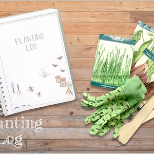 May include: A white gardening journal with the text "Planting Log" on the cover. The journal is open to a blank page. There are gardening gloves, wooden plant markers, and seed packets for asparagus and red onions on a wooden surface.