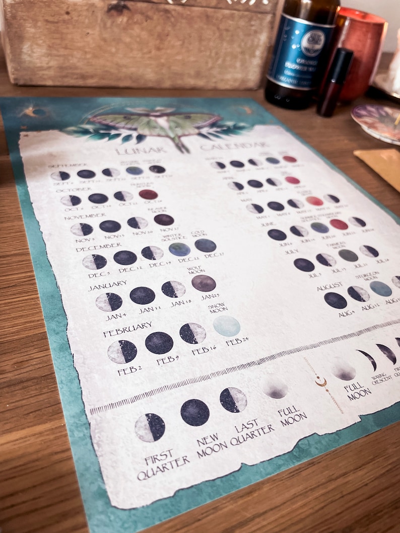 Pu&ograve; includere: Un calendario lunare color verde acqua e bianco con un'illustrazione di una falena. Il calendario mostra le fasi lunari per ogni mese dell'anno. Il testo sul calendario include i nomi dei mesi, le date delle fasi lunari e i nomi delle lune piene.