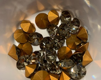 May include: A collection of gold and clear rhinestones in a bowl. The rhinestones are faceted and have a pointed top.