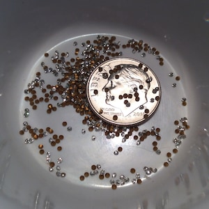 May include: A close-up of a US dime coin surrounded by small, clear and gold rhinestones. The coin is dated 2016 and has the words "In God We Trust" inscribed on it.