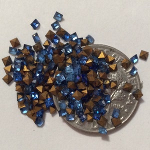 Peut inclure: Un tas de strass carrés bleus et dorés, certains avec une forme pyramidale, à côté d'une pièce de dix cents américaine.