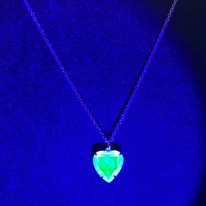May include: A silver chain necklace with a heart-shaped pendant. The pendant has a bright green, glowing center and a dark border. The background is a dark blue.