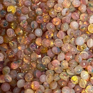 May include: A large quantity of iridescent glass beads in shades of pink, gold, and white. The beads are round and have a smooth, shiny finish.