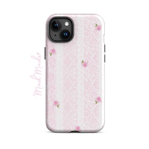 May include: A phone case featuring a pink lace design with small pink rose details. The case has a white border and a black camera module. The text "mad Made" is written in a cursive font on the left side of the case.