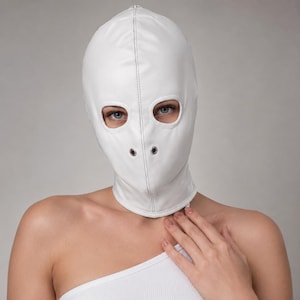 May include: A white full-head mask crafted from smooth material, featuring two oval-shaped eye openings and two small circular metal grommets positioned over the nose area. The mask has a central vertical seam and covers the entire head and neck.