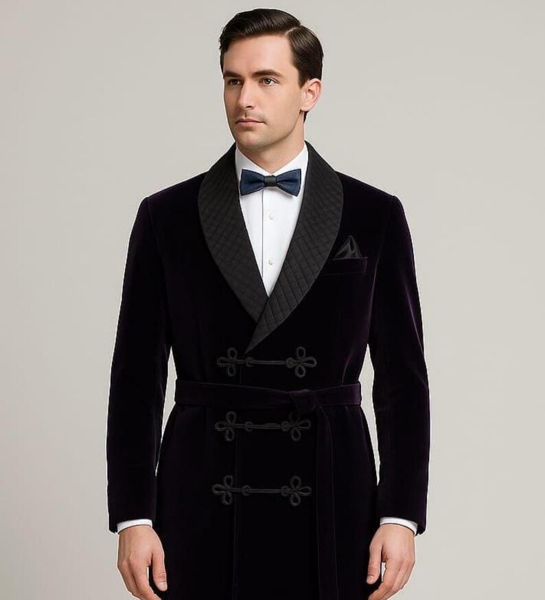 May include: A dark purple velvet robe with a quilted black lapel and a matching belt. The robe features decorative black frog closures and a small pocket. A white dress shirt and a navy bow tie are visible.
