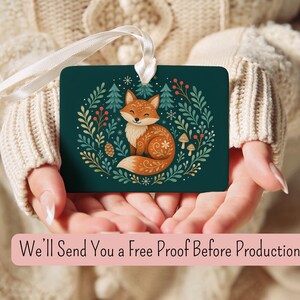 May include: A rectangular dark green ornament featuring a central illustration of a fox surrounded by pine trees, leaves, berries, and mushrooms. The ornament has a white ribbon loop at the top. The text reads: We'll Send You a Free Proof Before Production.