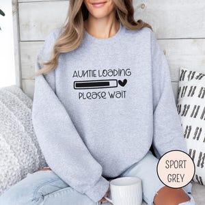 May include: Sport grey sweatshirt with the text "AUNTIE LOADING PLEASE WAIT" in black. The design includes a loading bar and a heart symbol. The sweatshirt is a light grey color.