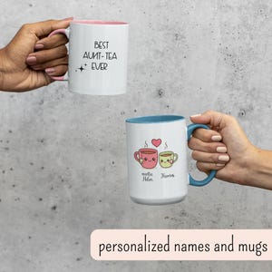 May include: Two white ceramic mugs with colorful accents. One mug has pink inside and handle, with the text "BEST AUNT-TEA EVER". The other mug has a blue handle and interior, with cartoon tea cups and names.