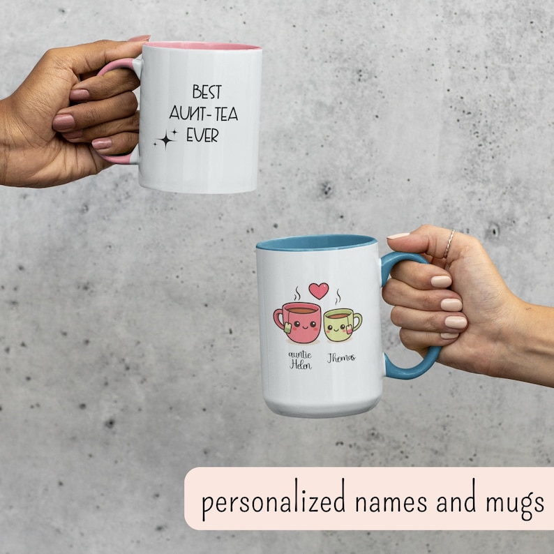 May include: Two white ceramic mugs with colorful accents. One mug has pink inside and handle, with the text "BEST AUNT-TEA EVER". The other mug has a blue handle and interior, with cartoon tea cups and names.