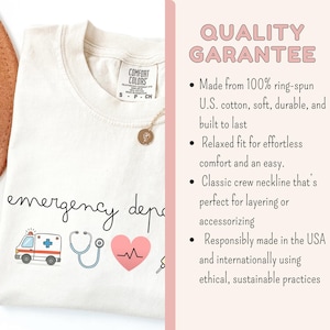 以下が含まれることがあります： クリーム色のTシャツ。筆記体で「emergency department」と書かれています。救急車、聴診器、心臓、鍵のイラストが描かれています。金のネックレスが見えます。このシャツは、100％リングスパン米国綿で作られています。