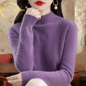 May include: A lavender-colored turtleneck sweater with long sleeves. The sweater has ribbed cuffs and a ribbed turtleneck collar. The image also includes the text "HavenHueBoutique" in a gold circular design.