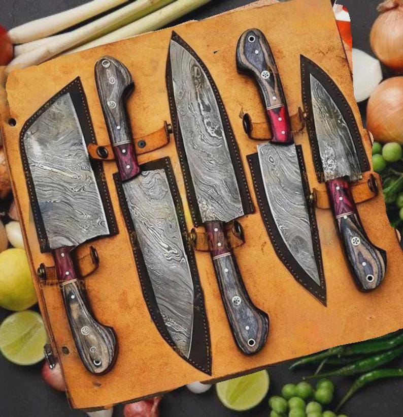 May include: A set of six Damascus steel kitchen knives with wooden handles and red accents, displayed in a brown leather sheath. The blades have a unique, wavy pattern. The knives are arranged on a wooden surface.
