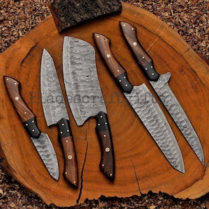 May include: A set of six Damascus steel knives with wooden handles and black accents. The blades have a unique patterned design. The knives are arranged on a wooden surface, showcasing their varying sizes and shapes, including a cleaver and a paring knife.