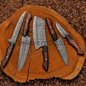 May include: A set of six Damascus steel kitchen knives with wooden handles and black accents. The blades have a unique patterned design. The knives are arranged on a round, wooden cutting board.
