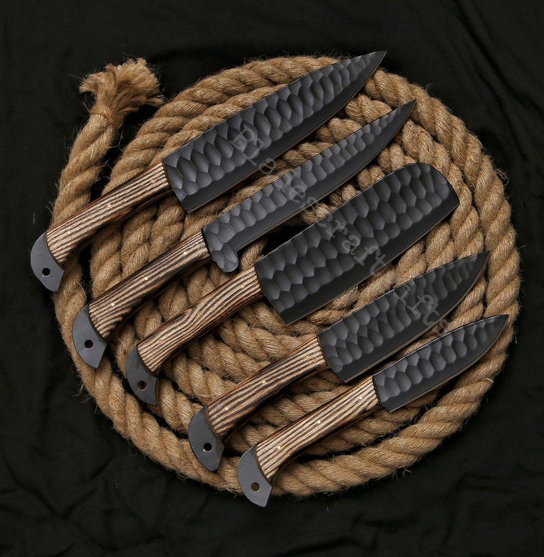 May include: A set of six black kitchen knives with textured blades and wooden handles. The knives are arranged on a coiled rope, showcasing their craftsmanship and design. The blades have a unique hammered texture.