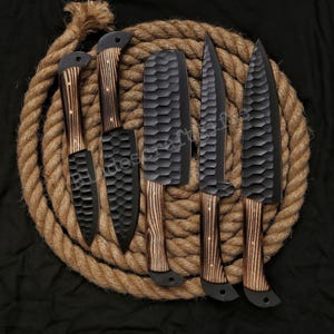May include: A set of five black kitchen knives with textured blades and wooden handles. The knives are arranged on a coiled rope against a black background. The handles have a light brown wood grain.