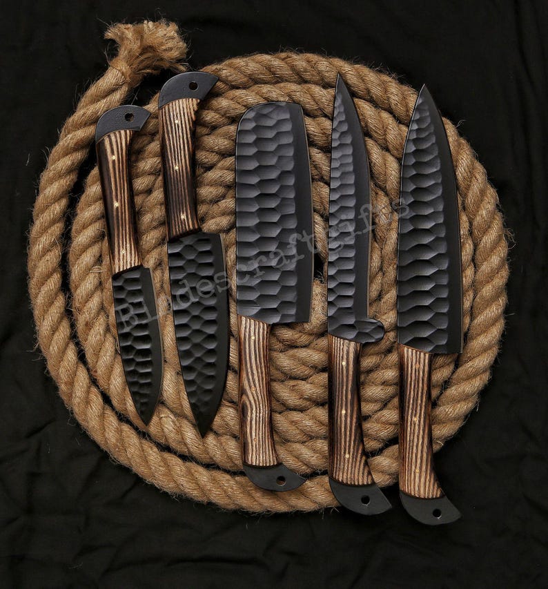 May include: A set of five black kitchen knives with textured blades and wooden handles. The knives are arranged on a coiled rope against a black background. The handles have a light brown wood grain.