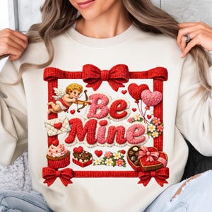 May include: Cream-colored sweatshirt with a Valentine's Day design. The design includes the words "Be Mine" in pink and red, a red bow border, a cupid, hearts, and sweets. The sweatshirt is a cozy and festive garment.