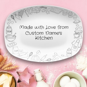 May include: White oval serving platter with a pink background. The platter has a border of sketched kitchen tools and the text "Made with Love from Custom Name's Kitchen" in the center. Baking-themed.