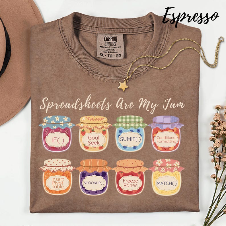 K&ouml;nnte beinhalten: Espressofarbenes T-Shirt mit dem Schriftzug "Spreadsheets Are My Jam" und Illustrationen von Marmeladengl&auml;sern, die jeweils mit Tabellenkalkulationsfunktionen beschriftet sind. Eine goldene Sternanh&auml;nger-Halskette liegt auf dem Shirt.