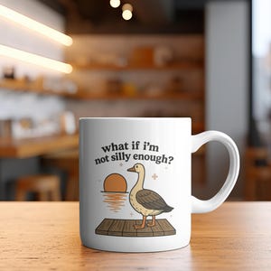 May include: White ceramic mug with a handle featuring a cartoon goose illustration. The goose stands on a wooden dock with a sunset in the background. Text on the mug reads "what if I'm not silly enough?"