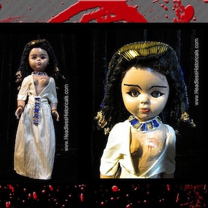 Puede incluir: Dos mu&ntilde;ecas vintage vestidas como faraones egipcios. Las mu&ntilde;ecas tienen cabello negro, ojos pintados y llevan vestidos de lino blanco con detalles dorados y azules. La mu&ntilde;eca de la derecha tiene una mancha roja en el pecho.
