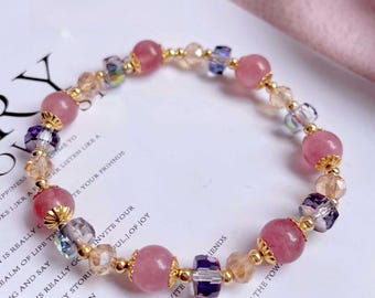 May include: A beaded bracelet featuring pink gemstone beads, gold-colored accents, and various crystal beads. The bracelet is strung on a flexible cord and is designed to be worn around the wrist. The bracelet is a piece of jewelry.