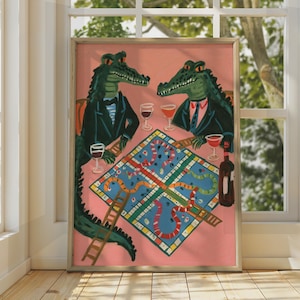 May include: A framed wall art print featuring two green crocodiles in dark suits sitting at a pink table playing a board game with snakes and ladders. The scene includes wine glasses and a bottle of wine on the table against a solid pink background.
