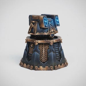 May include: A detailed miniature model of a futuristic structure. The model features a dark blue and bronze color scheme with intricate geometric designs. The top section has blue glowing lights, and the base has a hexagonal shape.