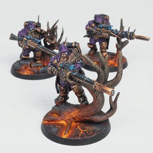 May include: Three miniature figures of fantasy warriors in purple armor and hooded cloaks, each holding a rifle. They stand on detailed bases with a lava-like texture and are surrounded by stylized tree-like structures.