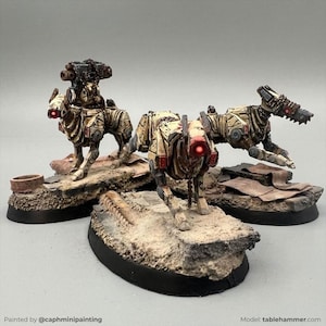 Può includere: Tre miniature di cani robotici, dipinte in tonalità beige e marrone, con occhi rossi luminosi. Ogni figura è montata su una base rocciosa strutturata. Una ha un'arma sulla schiena e un'altra un accessorio simile a un trapano.