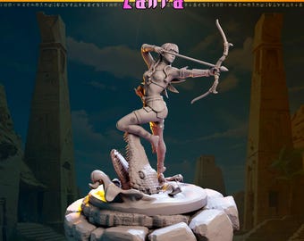 Puede incluir: Figurilla detallada de una arquera, con arco y flecha, de pie sobre una escultura de cocodrilo. La figura es de color claro, con la palabra "Zahra" en rosa arriba. El fondo presenta estructuras de estilo egipcio antiguo.