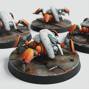 Puede incluir: Figuras de robots en miniatura con detalles en naranja, blanco y turquesa. Los robots tienen un diseño similar a una araña y están montados sobre bases circulares con una apariencia metálica desgastada. Los robots están sobre un fondo blanco.