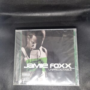 May include: A CD case featuring Jamie Foxx's album "Unpredictable." The cover art shows a black and white image of Jamie Foxx holding a microphone, with the album title and artist's name in white and green text. The CD case has a parental advisory sticker.
