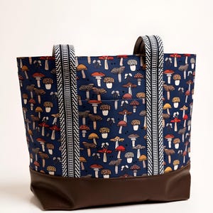 May include: A tote bag with a dark blue mushroom pattern. The bag has a brown leather bottom and handles with a black and white chevron design. The bag has a pocket on the front.