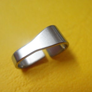 Könnte beinhalten: Ein silberner Metallring mit glatter, polierter Oberfläche. Der Ring ist an einer Seite offen und hat eine gebogene Form.