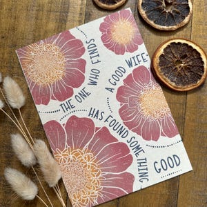 May include: A greeting card with a floral design and the text "The one who finds a good wife has found some thing good." The card is surrounded by dried orange slices and dried flowers.